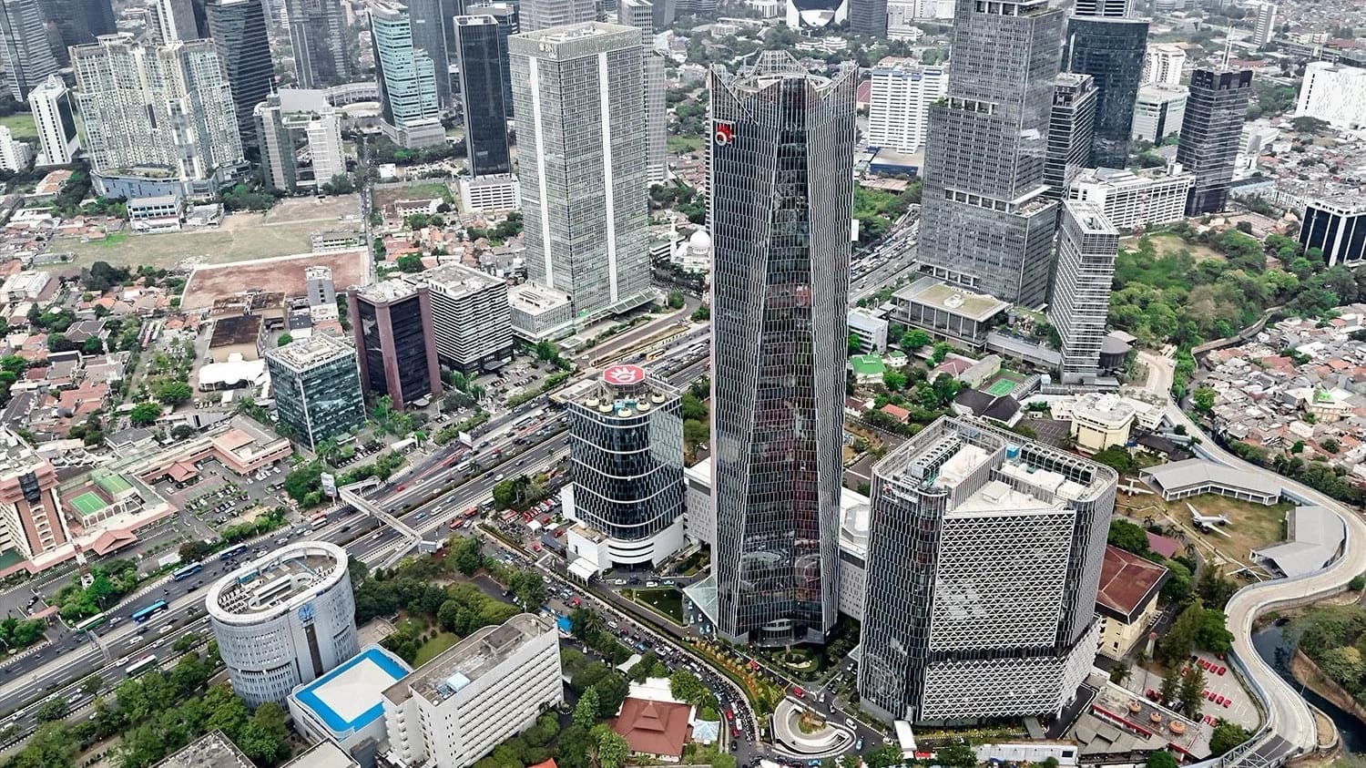 Pemandangan udara kawasan bisnis perkotaan yang padat dengan gedung-gedung pencakar langit berlapis kaca, jalan tol berlajur banyak, dan permukiman rendah di sekitarnya.
