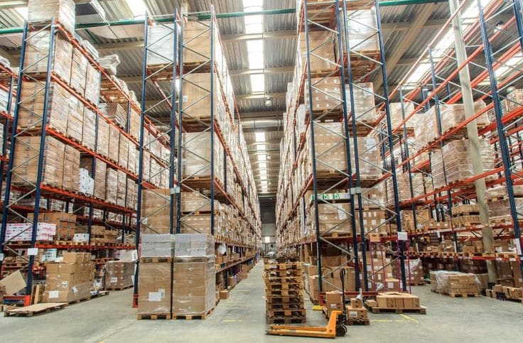 Lorong gudang dengan rak palet tinggi berisi barang